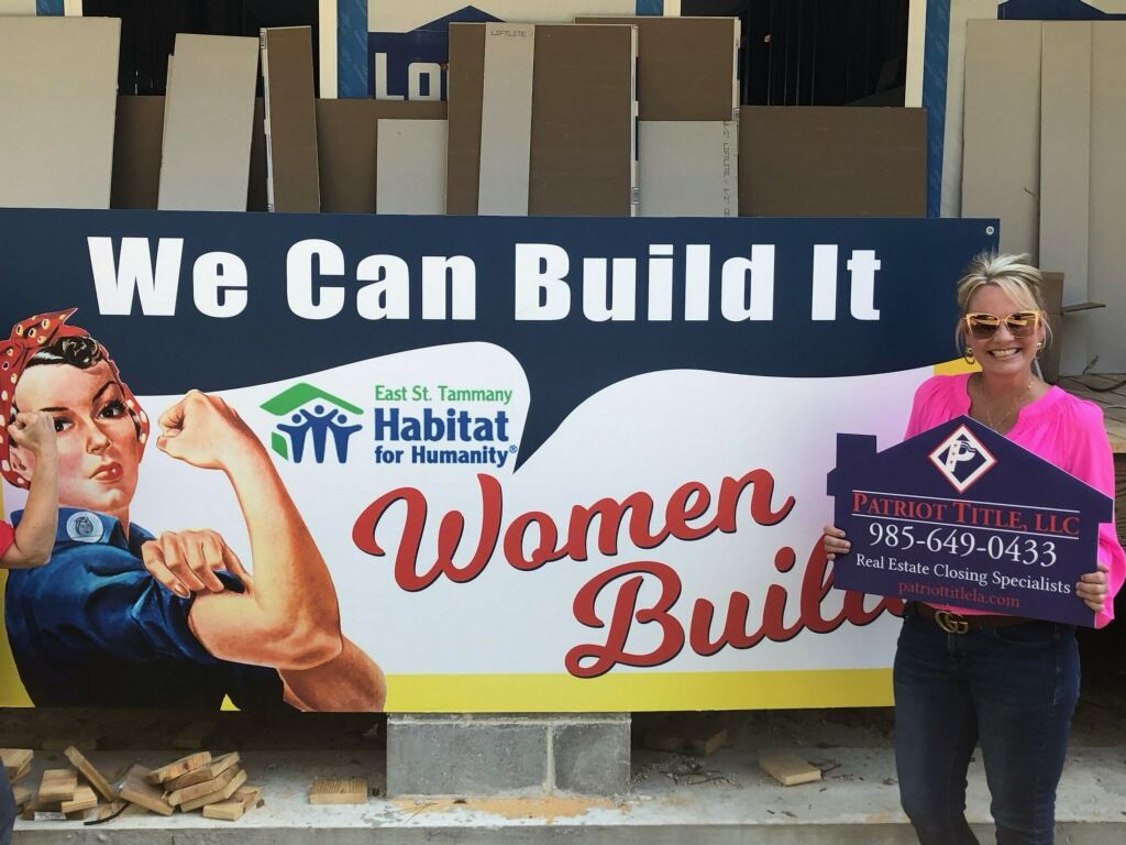 A Patriot Title team member with a Patriot Title sign at the East St. Tammany Habitat for Humanity Women Build